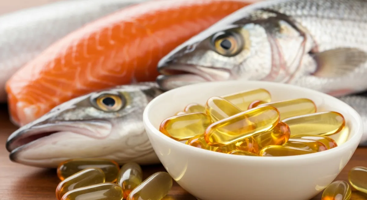 Capsules d'huile de poisson oméga 3 dans un bol en verre avec du poisson frais en arrière-plan